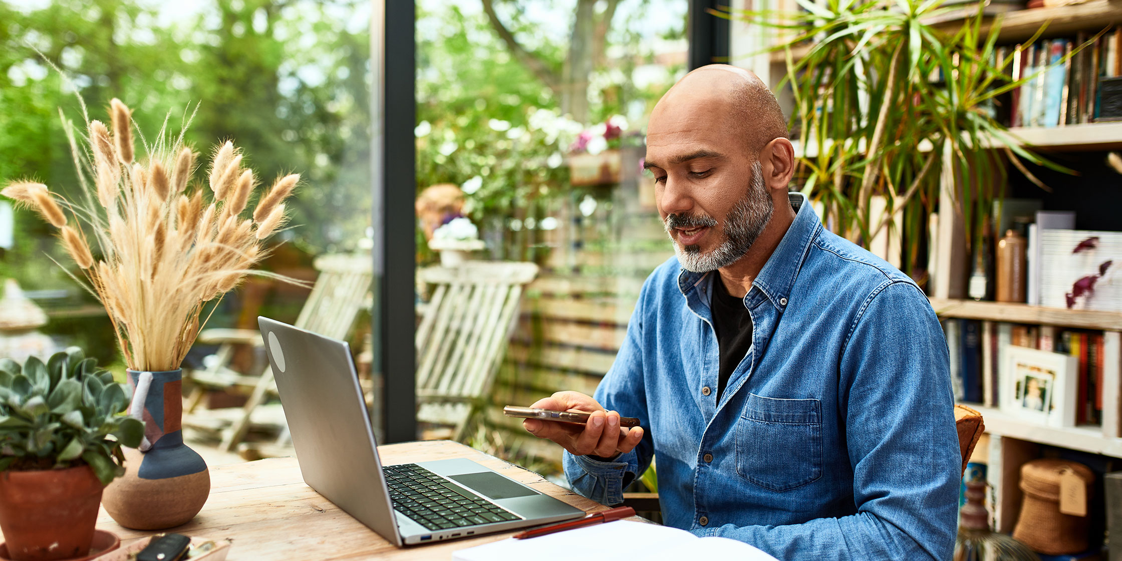 Man inside a house talking on speakerphone while using a laptop.