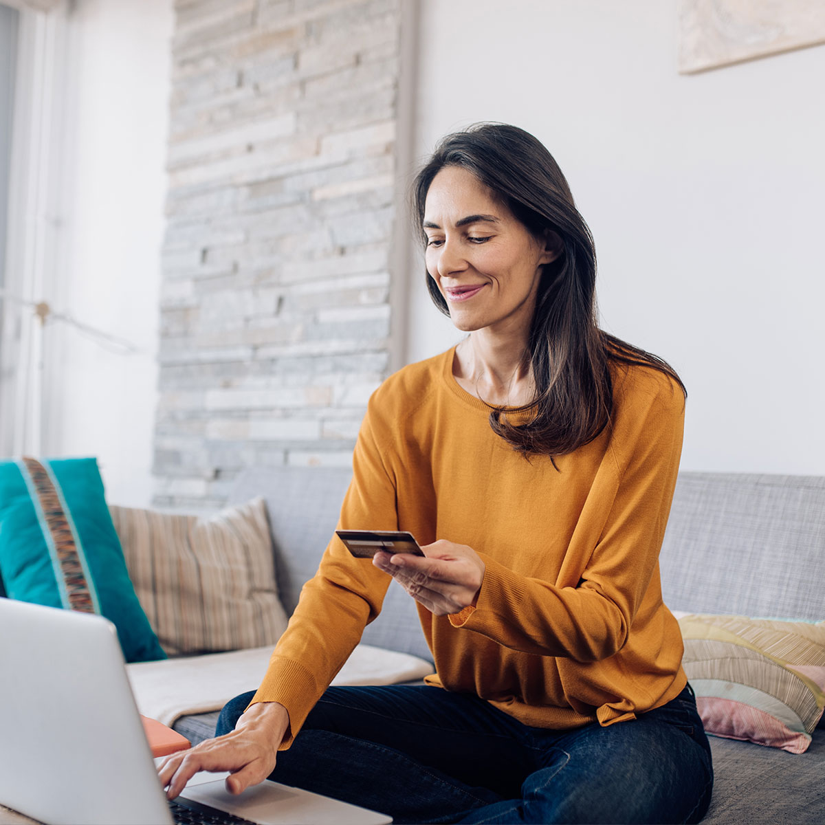 A photo of a woman holding a credit card while using her laptop.