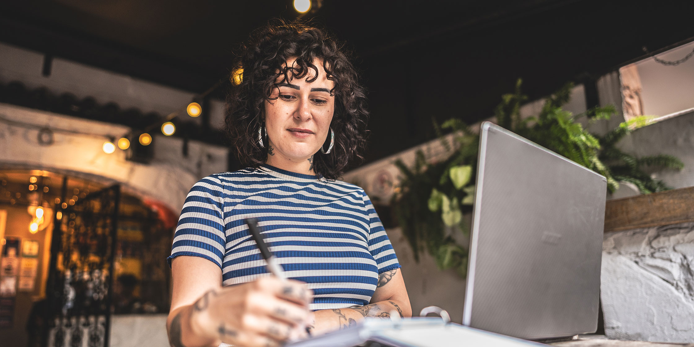 A smiling woman writing while working at a laptop.