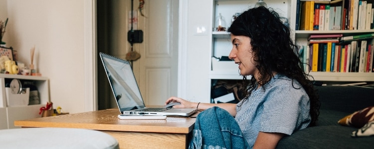 A woman sits at her desk and uses her laptop to check her credit scores.