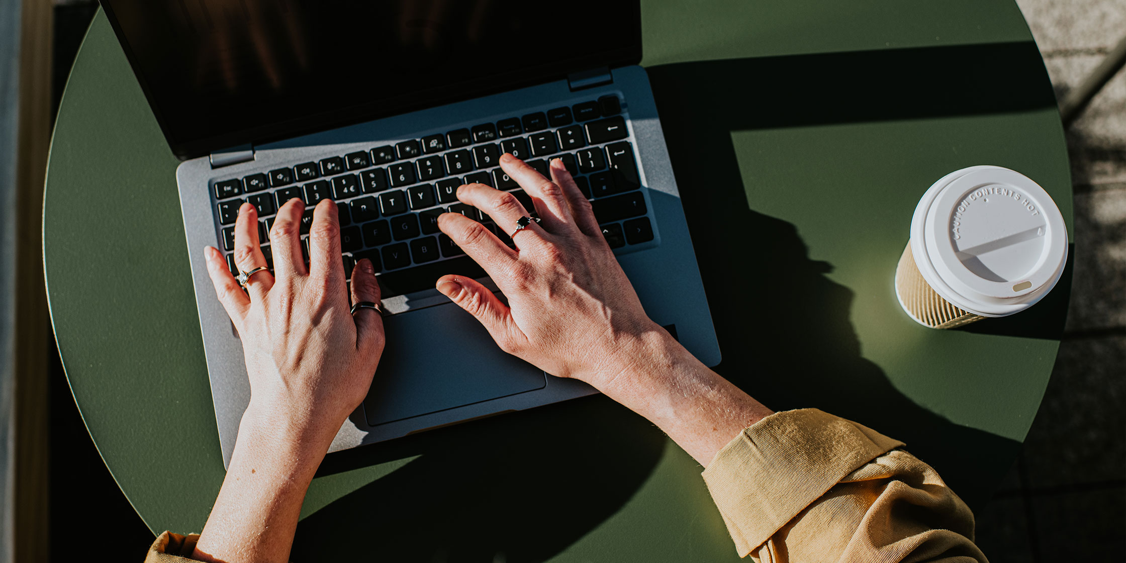 A person typing on their laptop with their coffee sitting on the table.